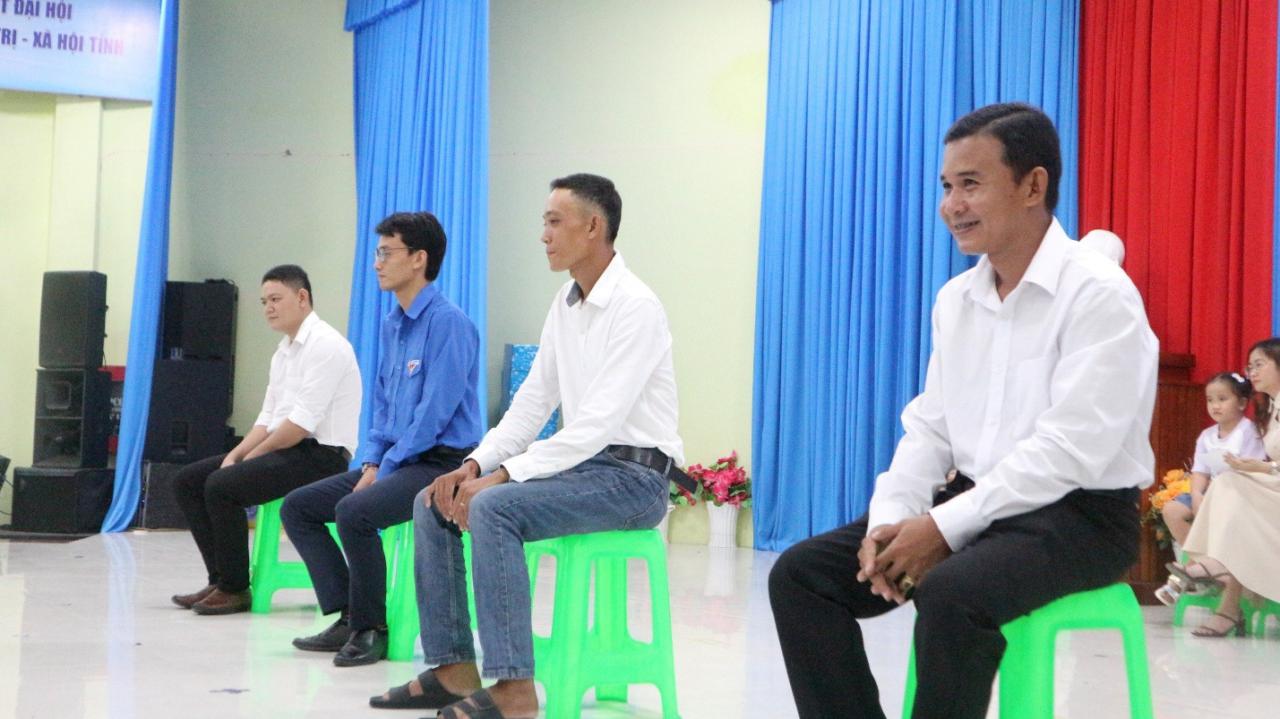 A group of men sitting on green stools Description automatically generated