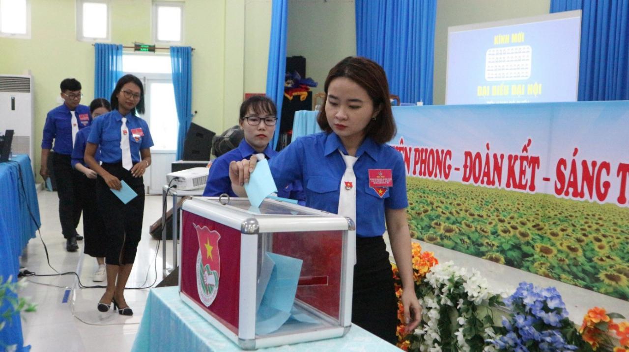 A person putting a piece of paper into a ballot box

Description automatically generated