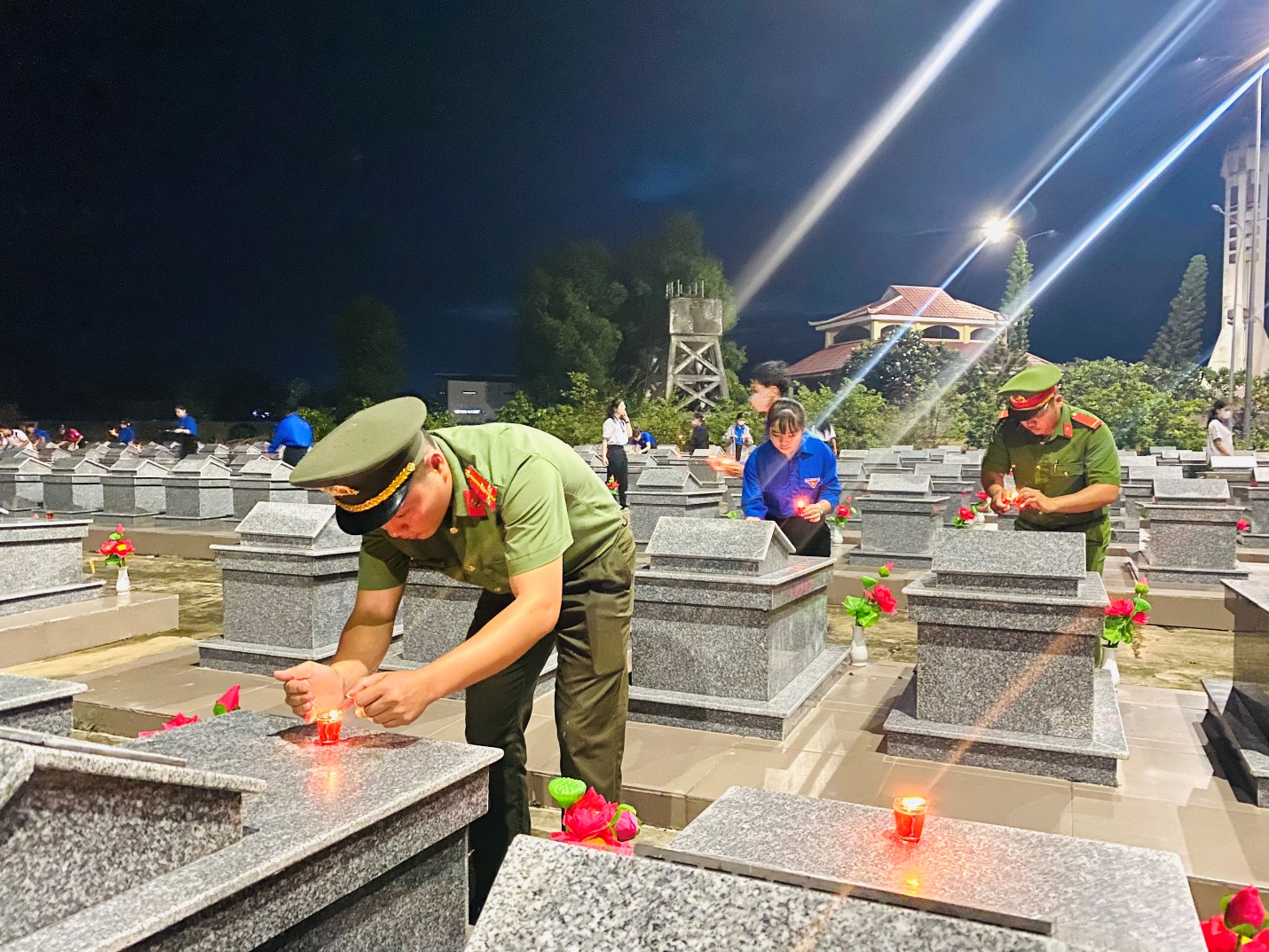 A group of people in military uniforms lighting candles on gravestones Description automatically generated