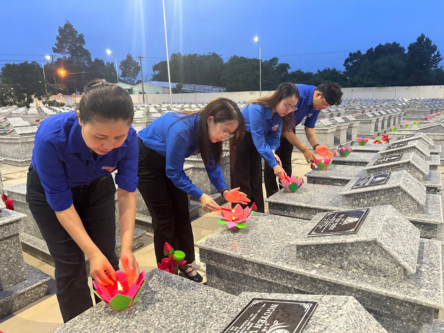 A group of people lighting flowers at a cemetery Description automatically generated
