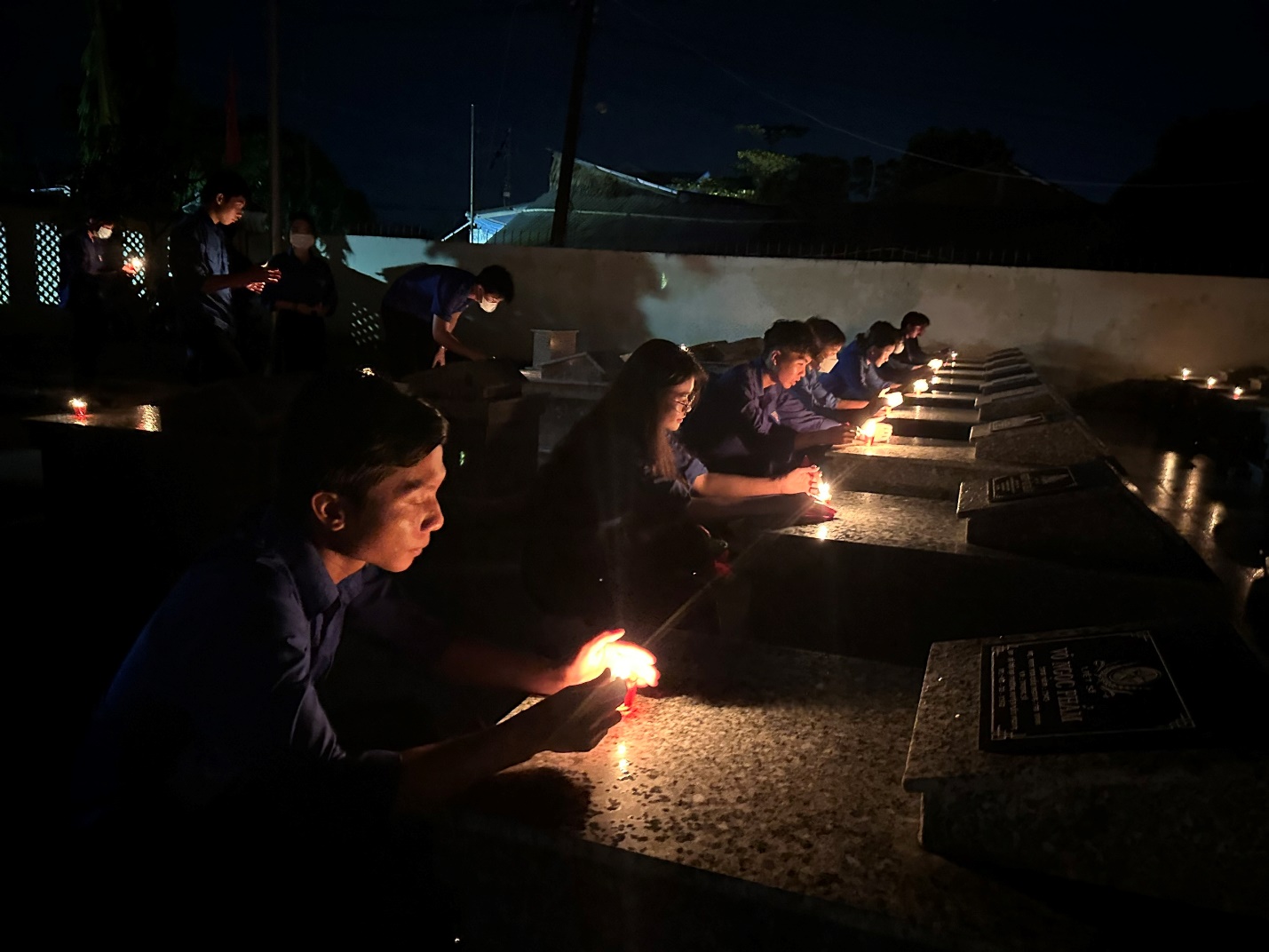 A group of people sitting at a grave Description automatically generated
