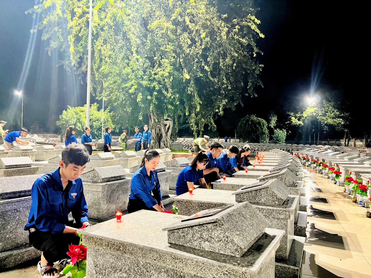 A group of people sitting at a grave Description automatically generated
