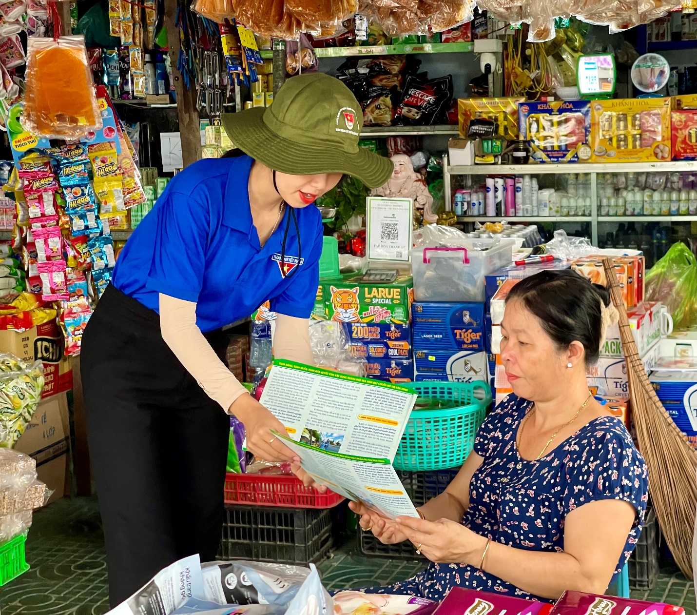 A person in a hat reading a book to a person in a store Description automatically generated