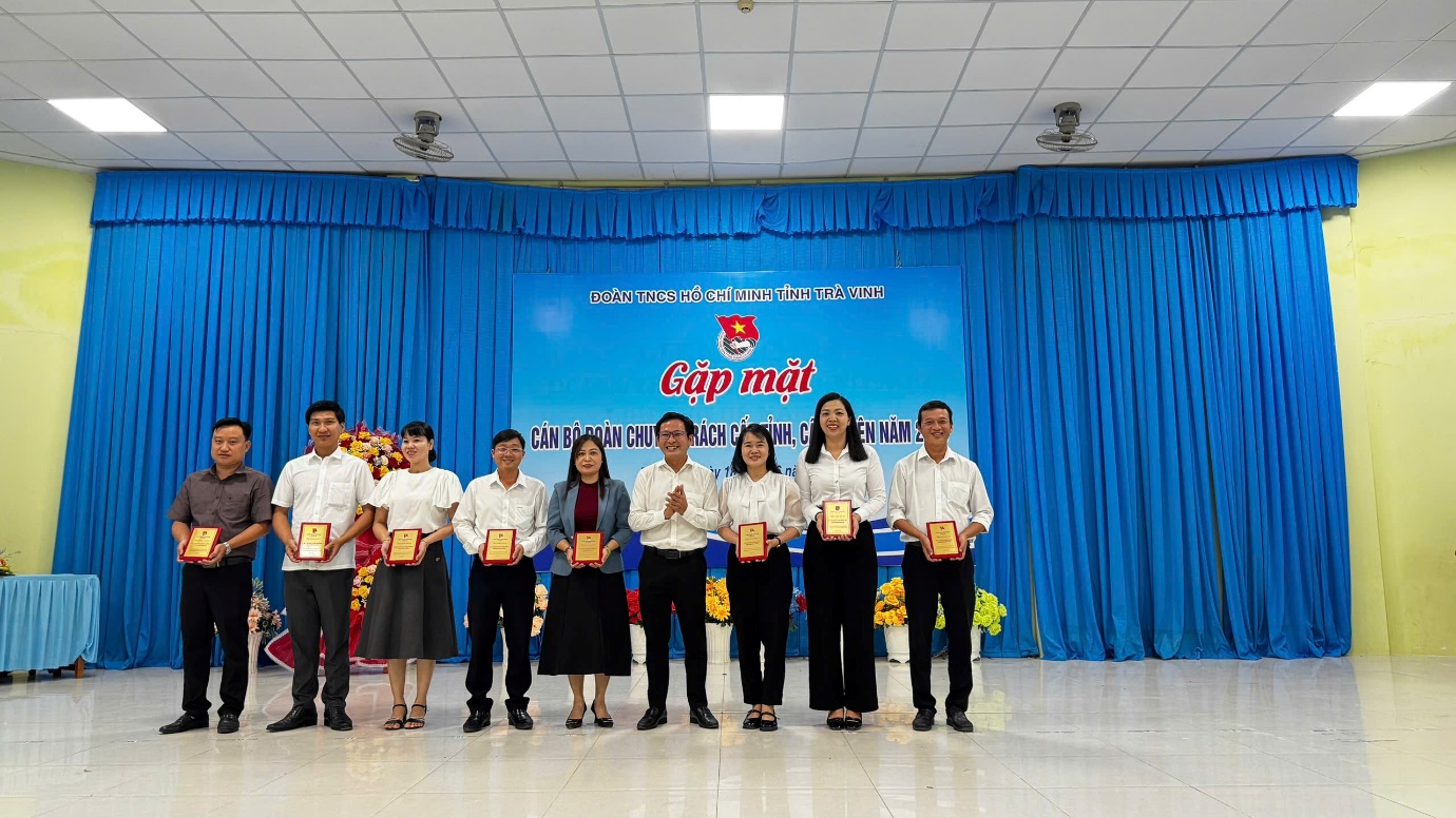 A group of people standing in front of a blue curtain
Description automatically generated