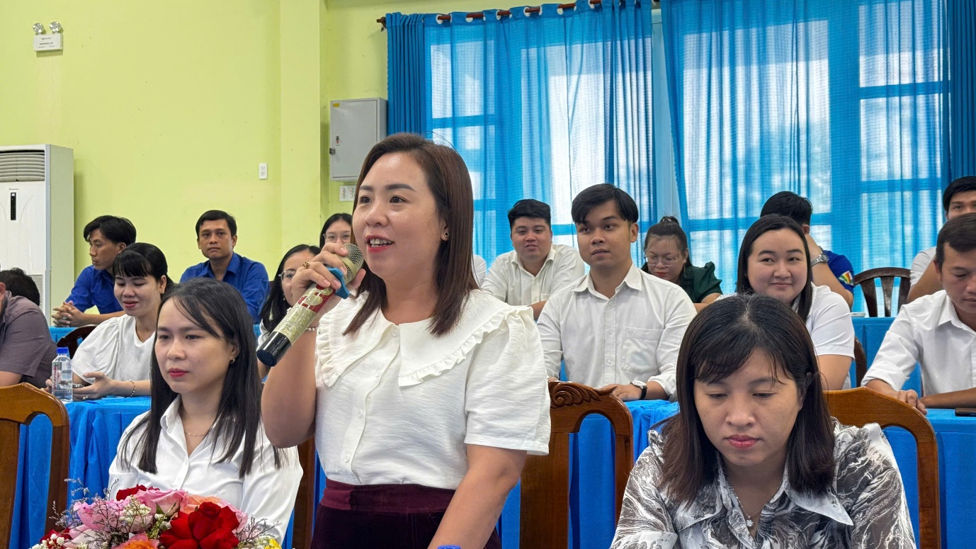 A person holding a microphone in front of a group of people
Description automatically generated